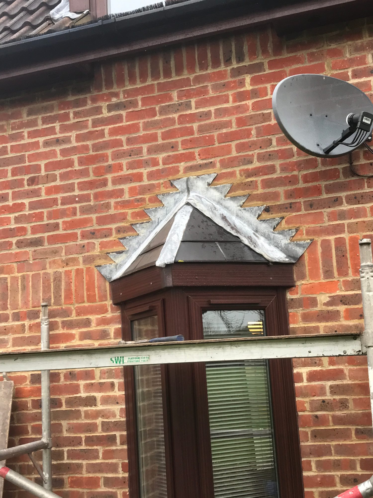 Close-up of existing leadwork around the pitched roof above a bay window, with overlapping lead sheets visible against the brickwork