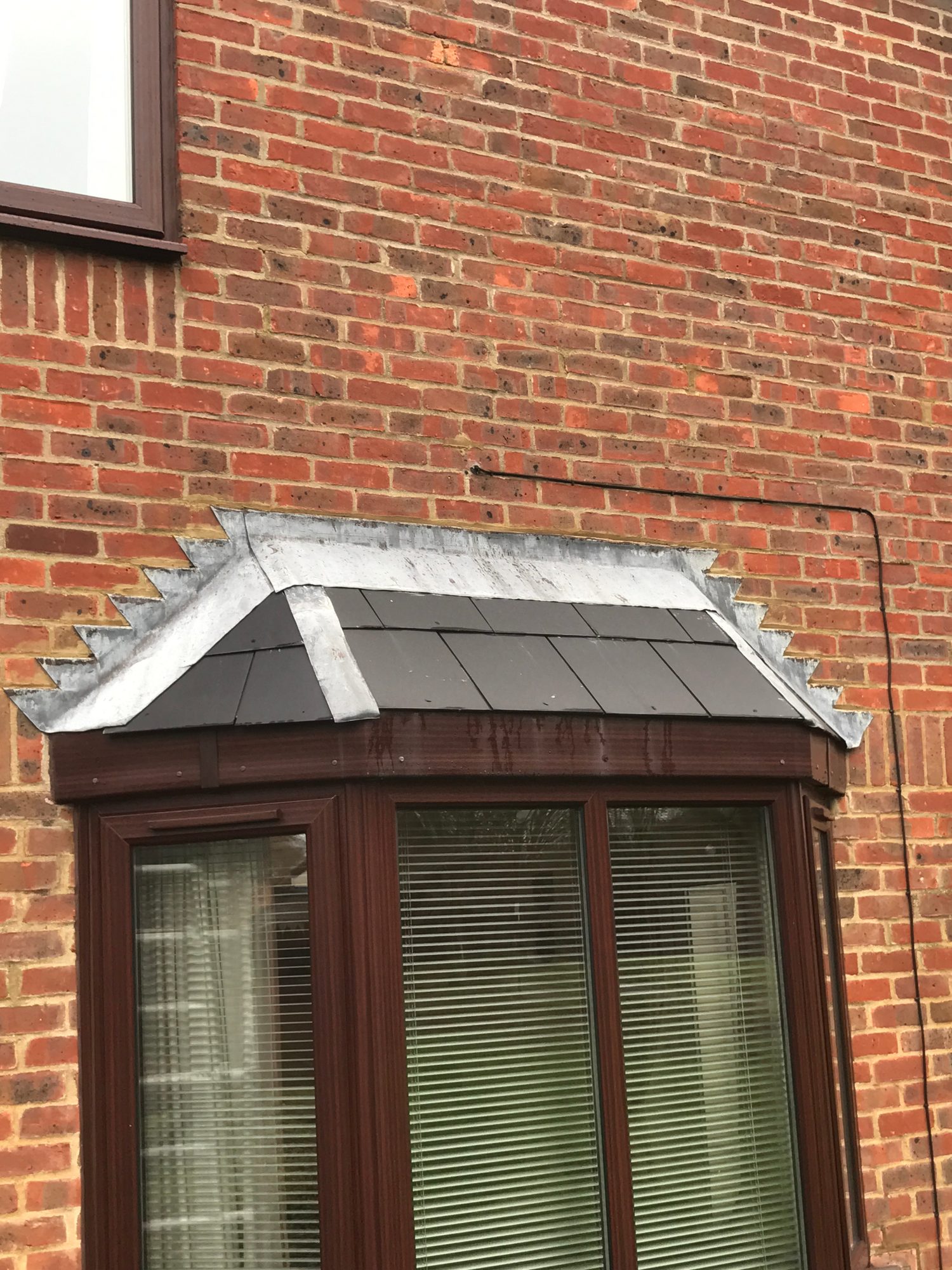 Front view of the bay window roof showing existing lead flashing across the roof edge and against the surrounding brick wall