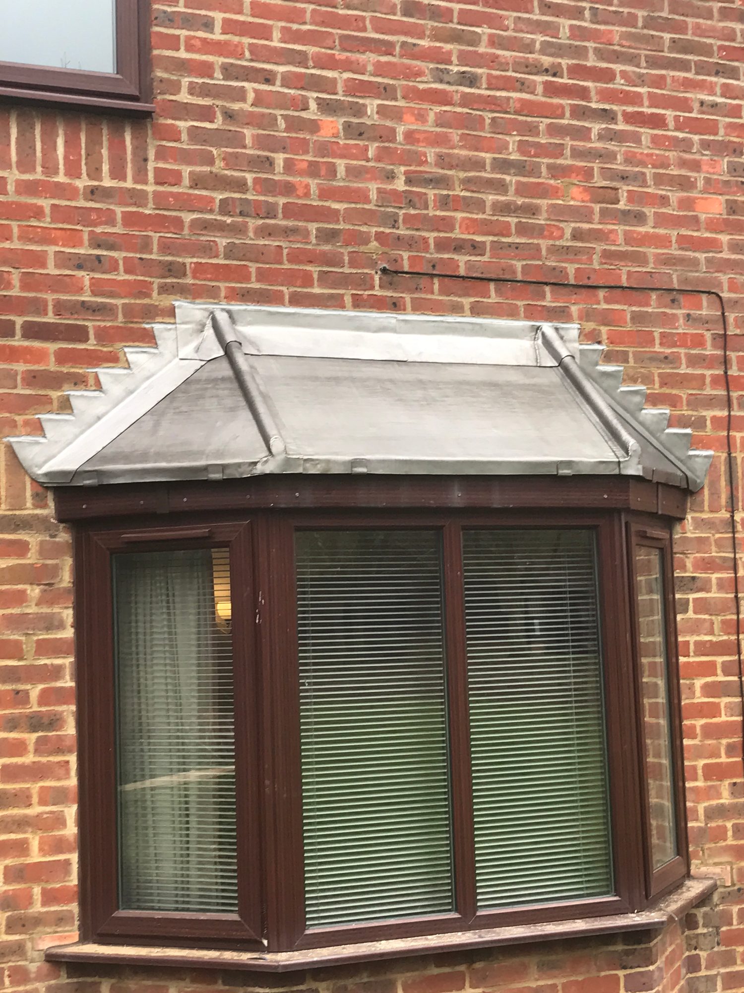 Completed lead-covered bay window roof with two lead rolls, stepped flashing and a clean finished appearance