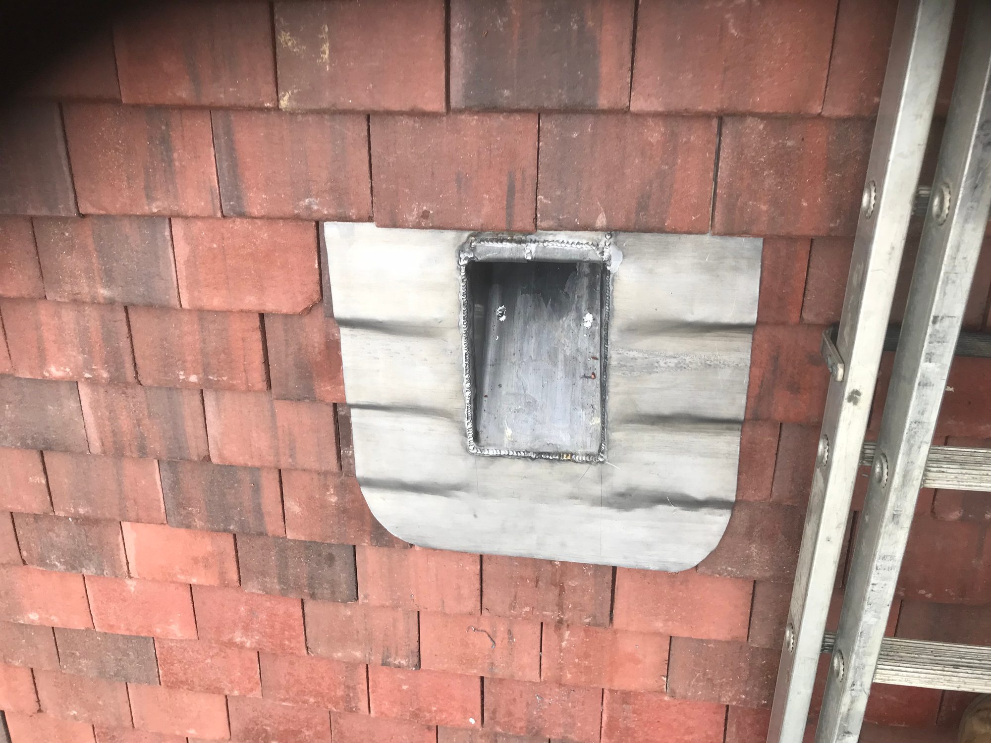 Close-up of a bespoke lead roof outlet set into a red brick wall, with formed leadwork surrounding the rectangular opening