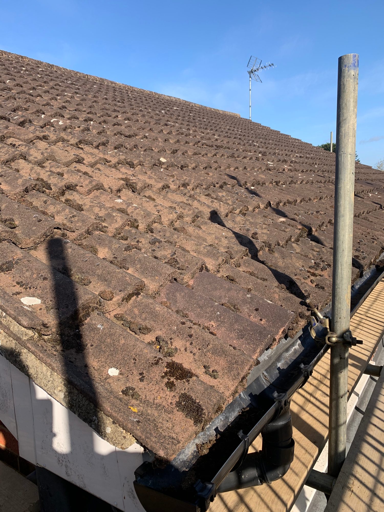 Close view of the existing pitched roof covered with weathered slate tiles, with moss and surface deterioration visible across the roof and scaffolding along the roof edge