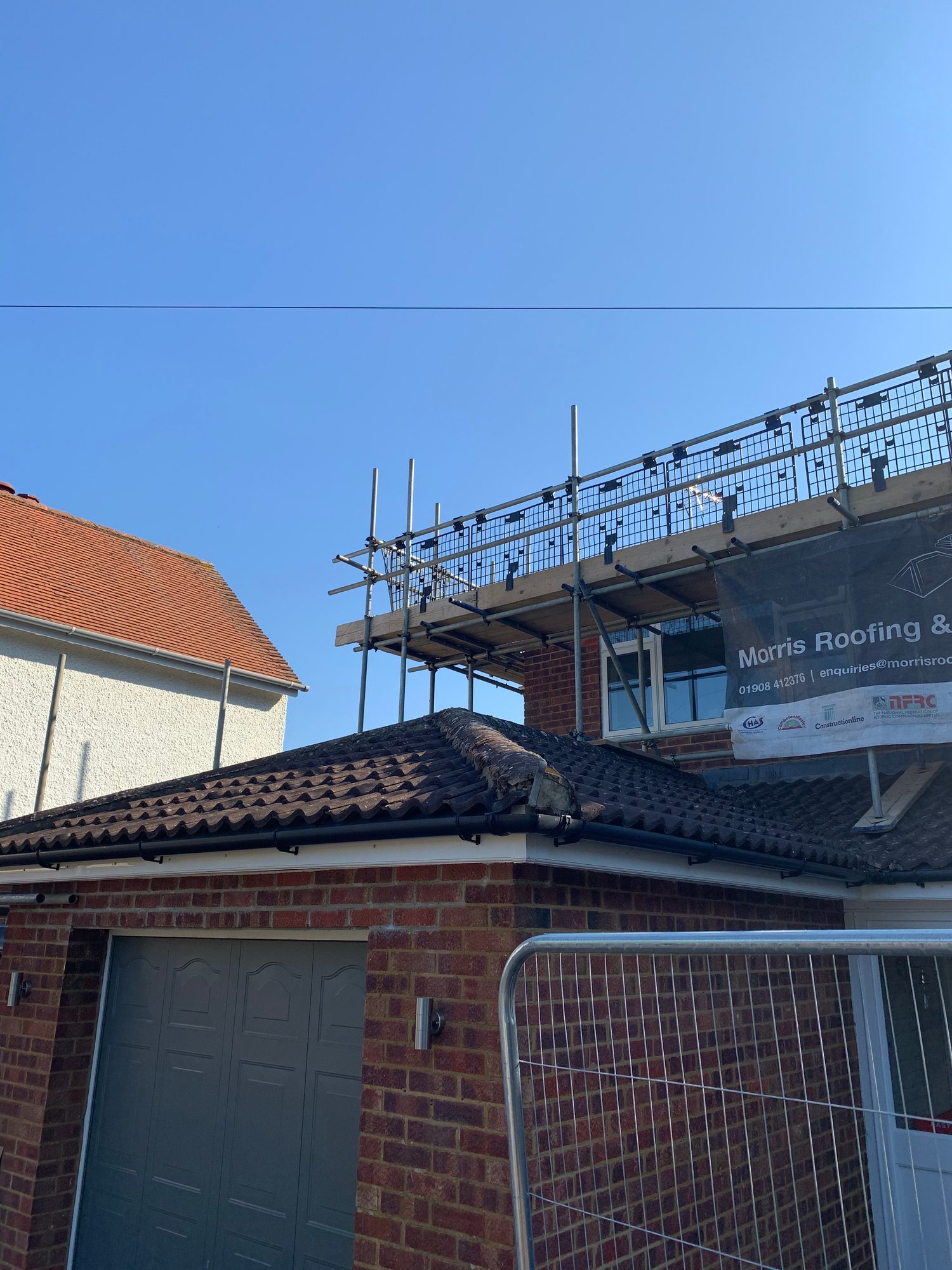 View of the existing roof showing weathered dark tiles, the roof hip and guttering, with scaffolding erected around the adjoining building and roof area