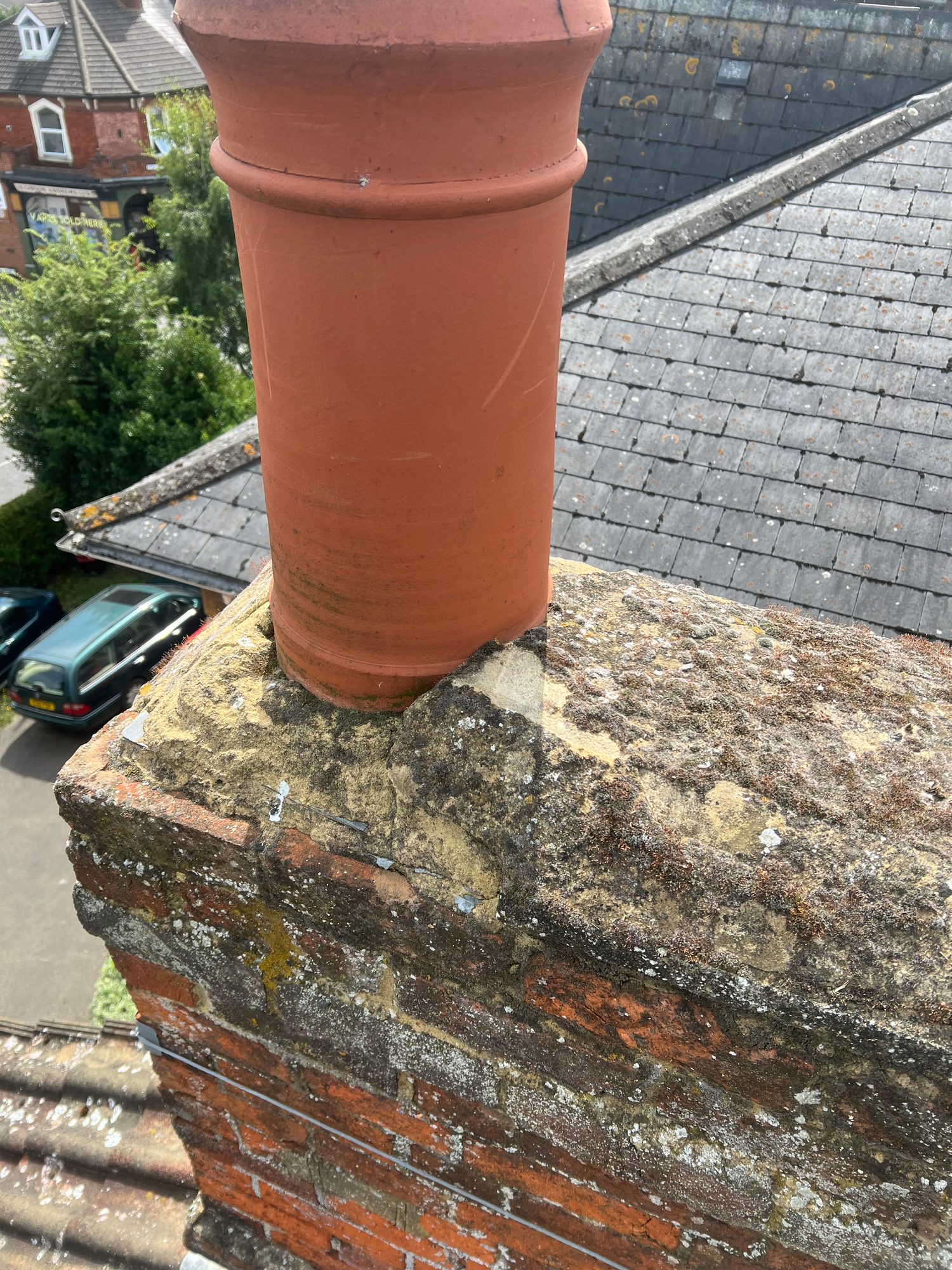 Before - The chimney showing moss and lichen growth across the brickwork and chimney pot, with the tiled roof visible behind