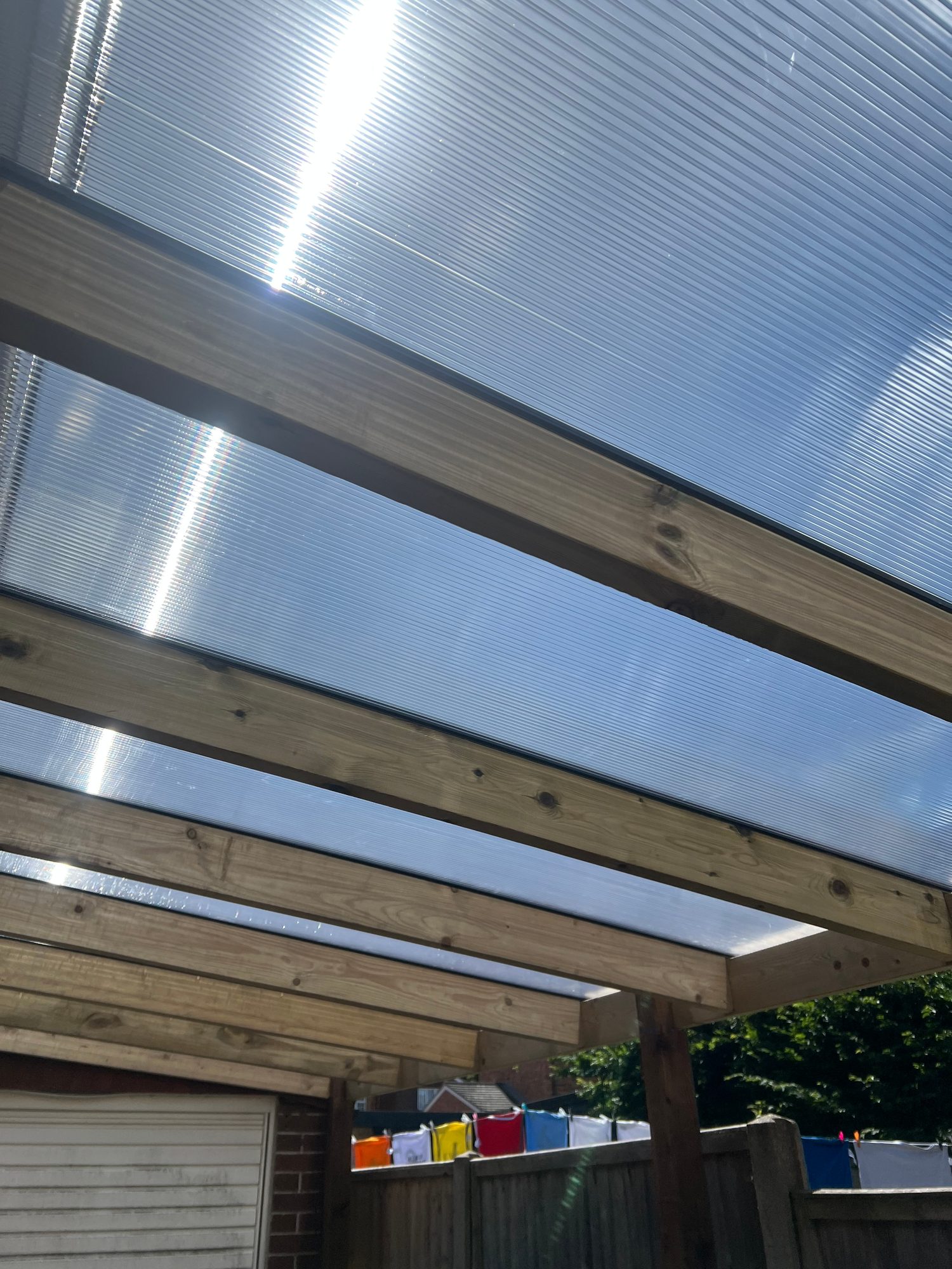 Completed garden shelter showing timber roof beams and translucent corrugated roof panels allowing natural light through