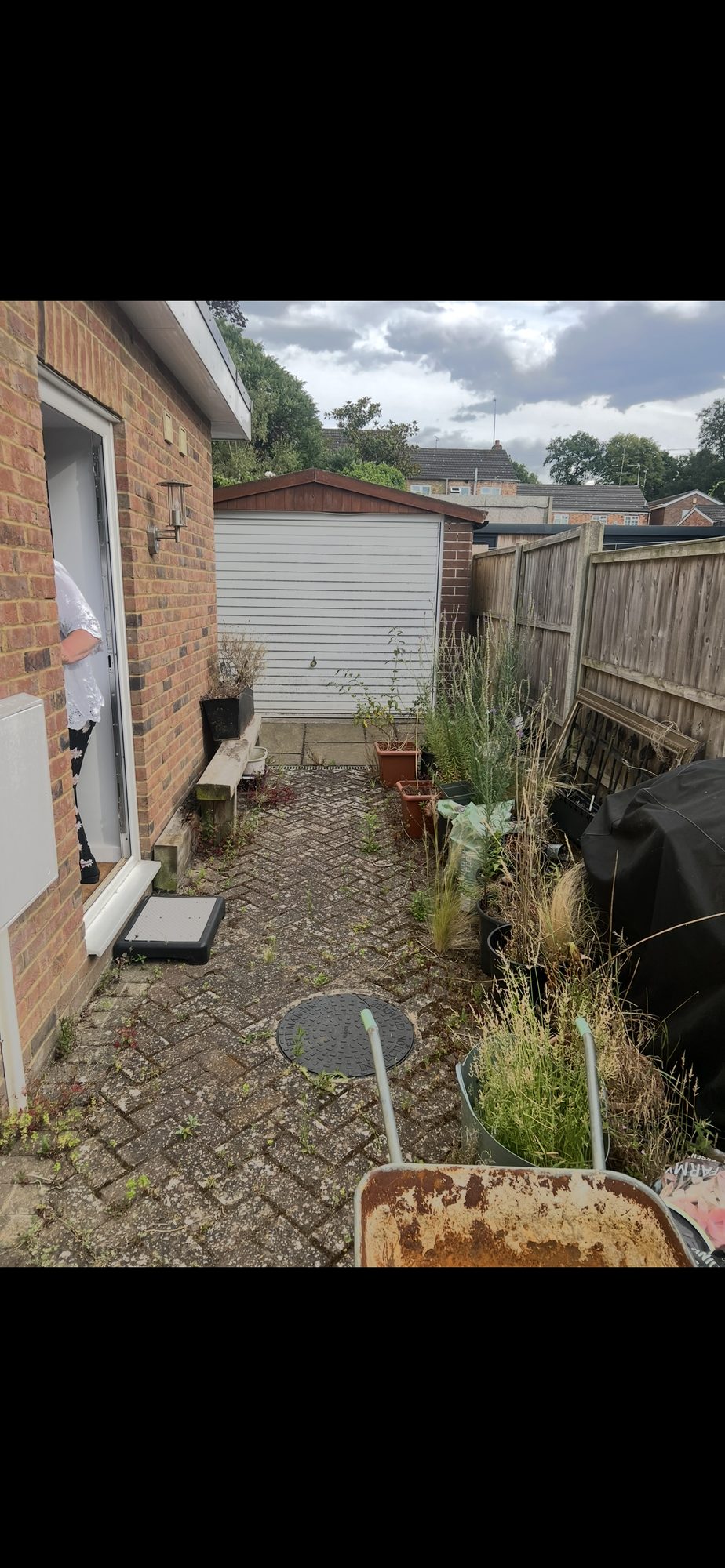 Existing paved garden area beside a brick house, with a garage and timber fencing