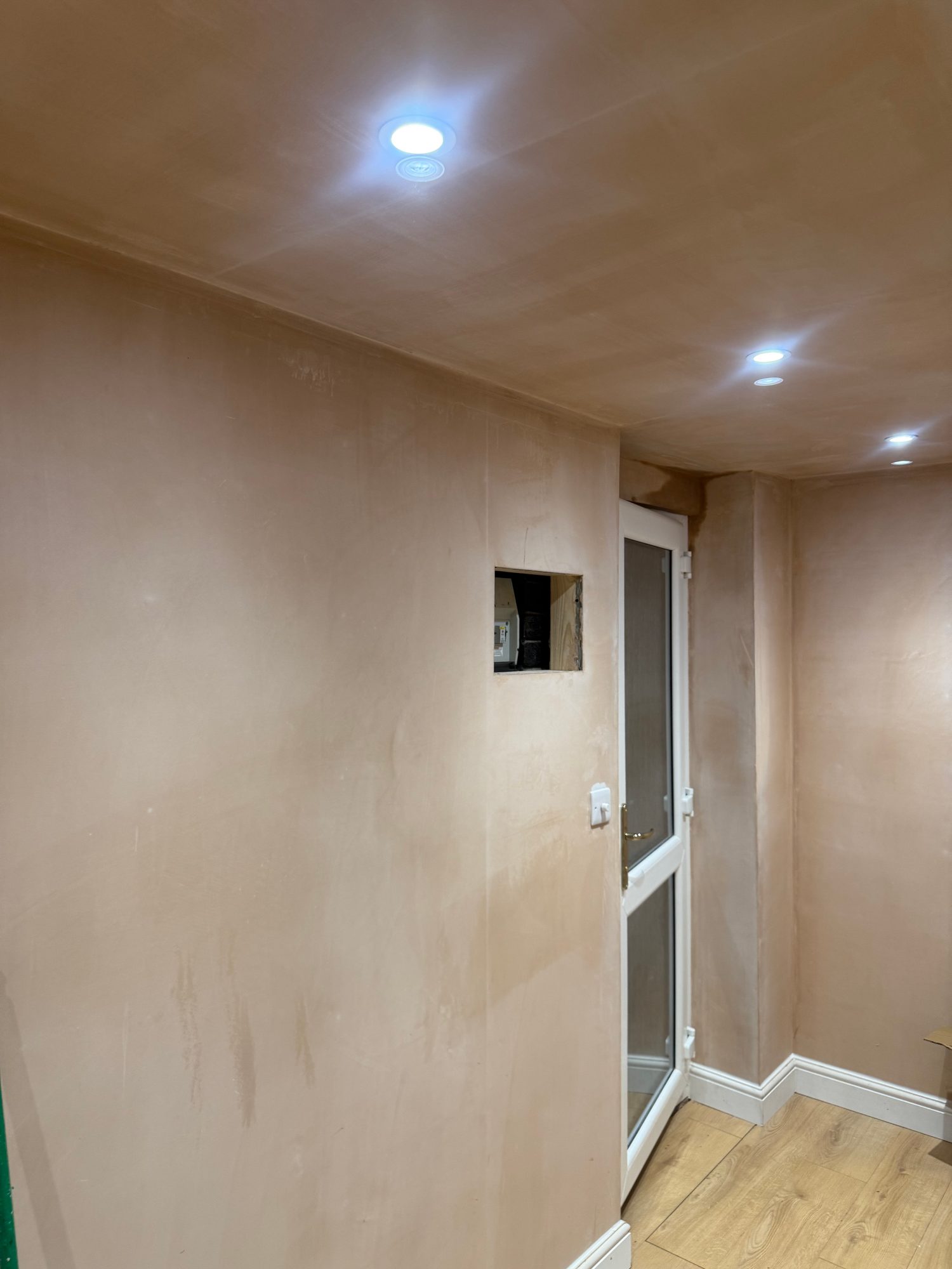 Interior room showing finished wall surfaces, wood-effect flooring, white skirting boards, a glazed door and multiple recessed ceiling lights