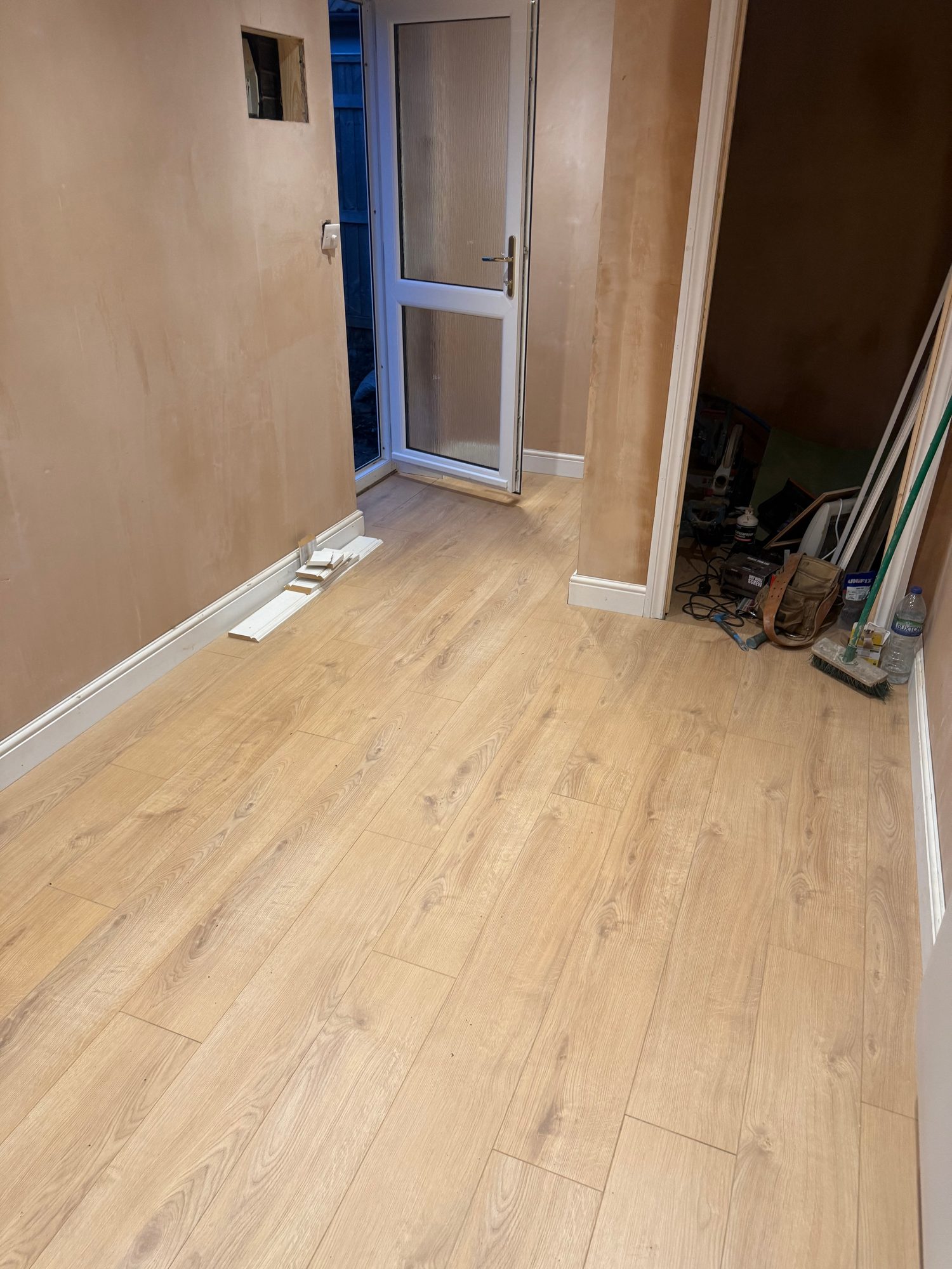 Interior showing newly laid wood-effect flooring, white skirting boards, finished wall surfaces and a white glazed door