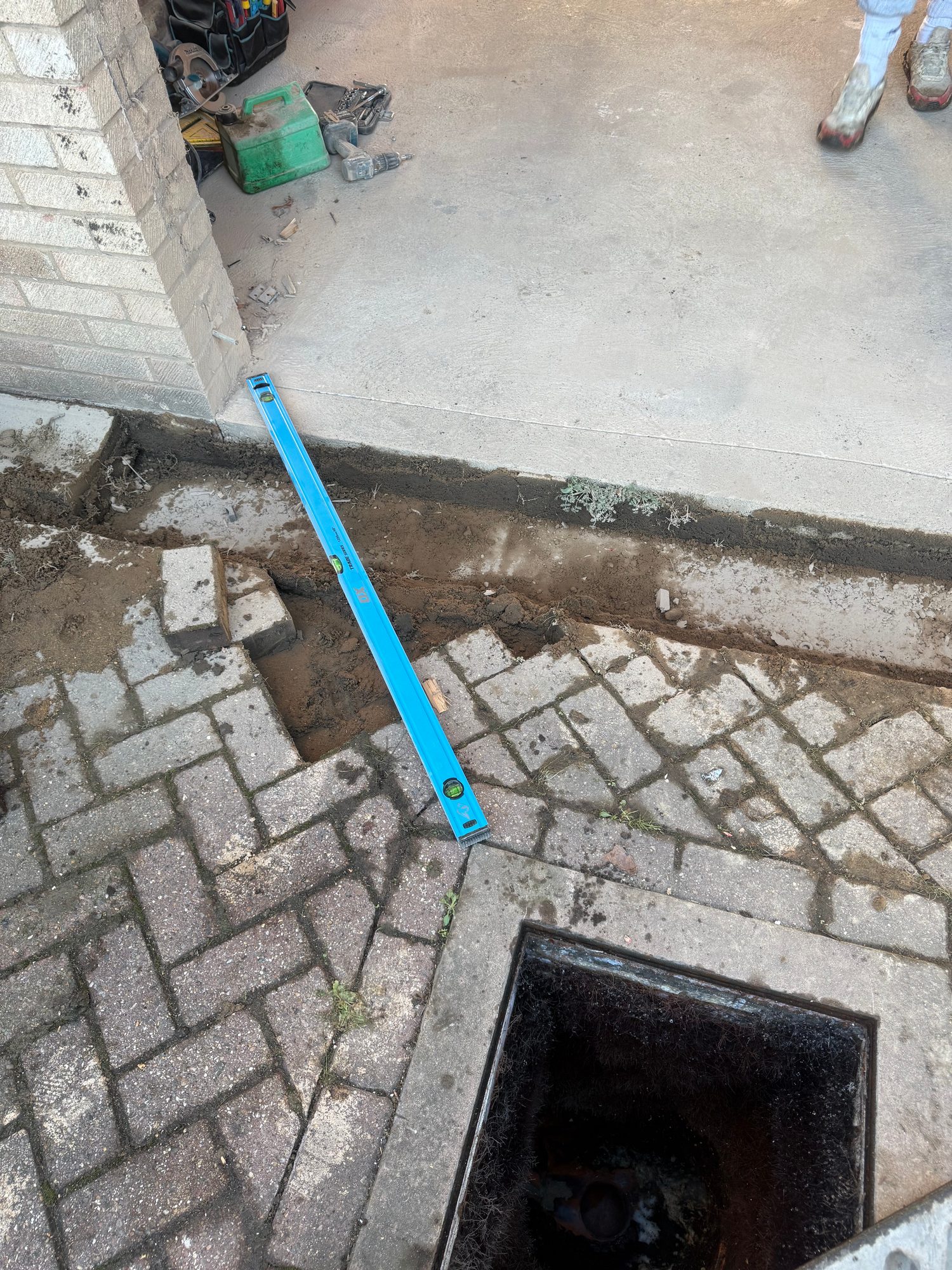 Concrete garage entrance beside a section of excavated ground and paving, with a spirit level and tools visible on site