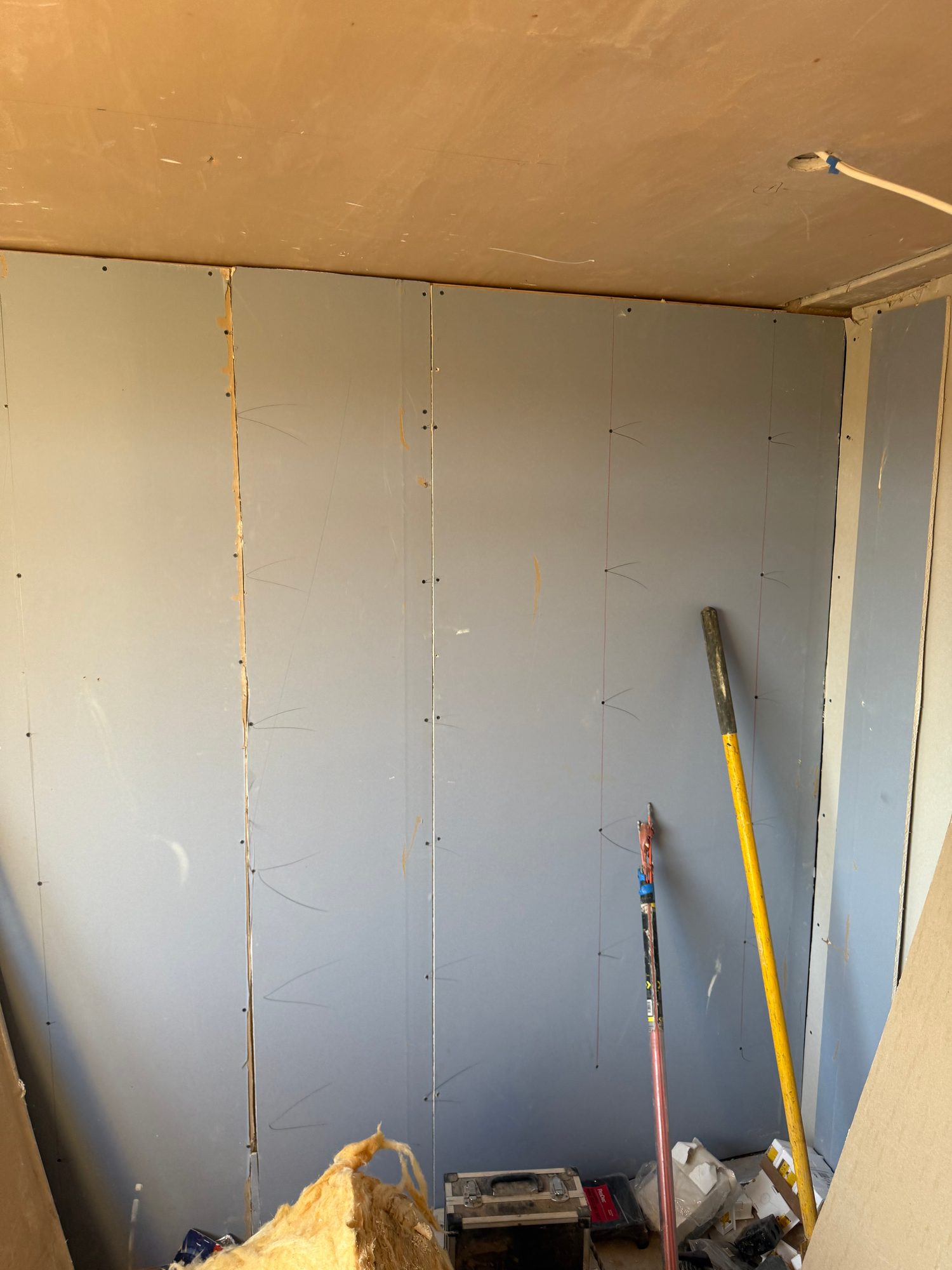 Interior room with plasterboard sheets fixed to the walls and ceiling, with tools and insulation visible on the floor