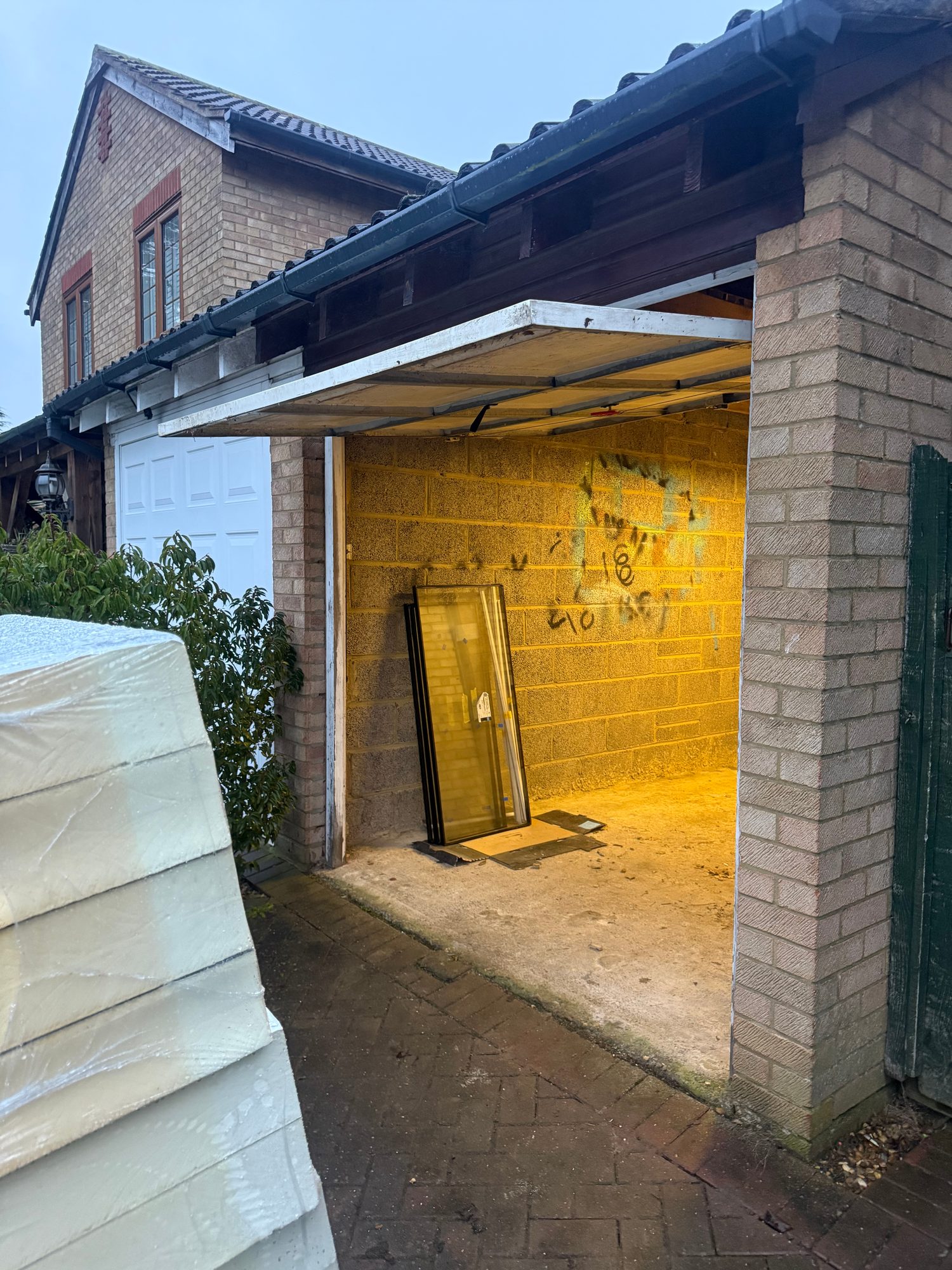 Open garage door showing the blockwork interior, with a door panel visible inside the garage and a second white garage door to the left