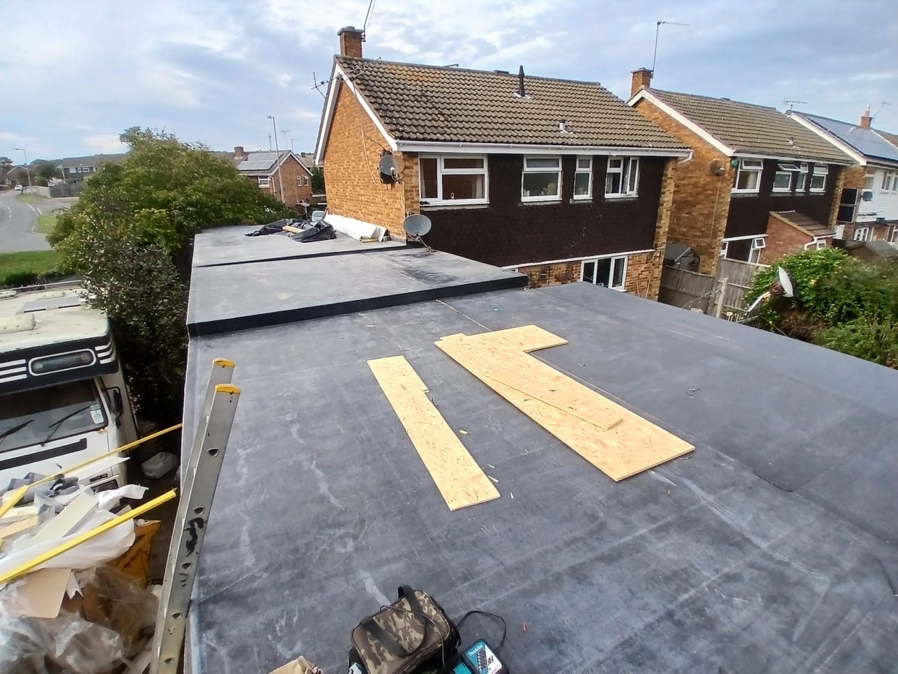 View across a flat roof under installation, with roofing materials and timber boards on the surface